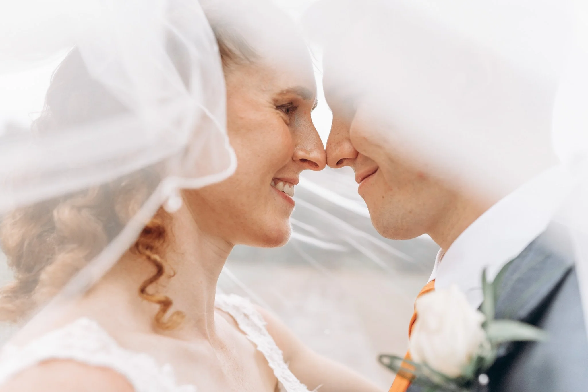 Bride and groom sharing an intimate kiss beneath a flowing veil at golden hour